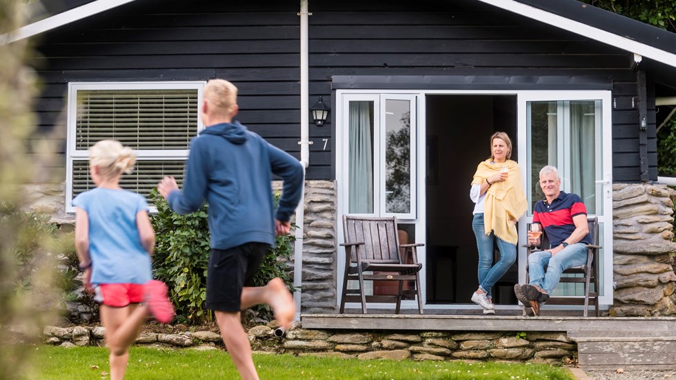 Two children run on the lawn of Furneaux Lodge while their parents enjoy a glass of wine on the deck of their Cook's Cottage in the Marlborough Sounds, New Zealand