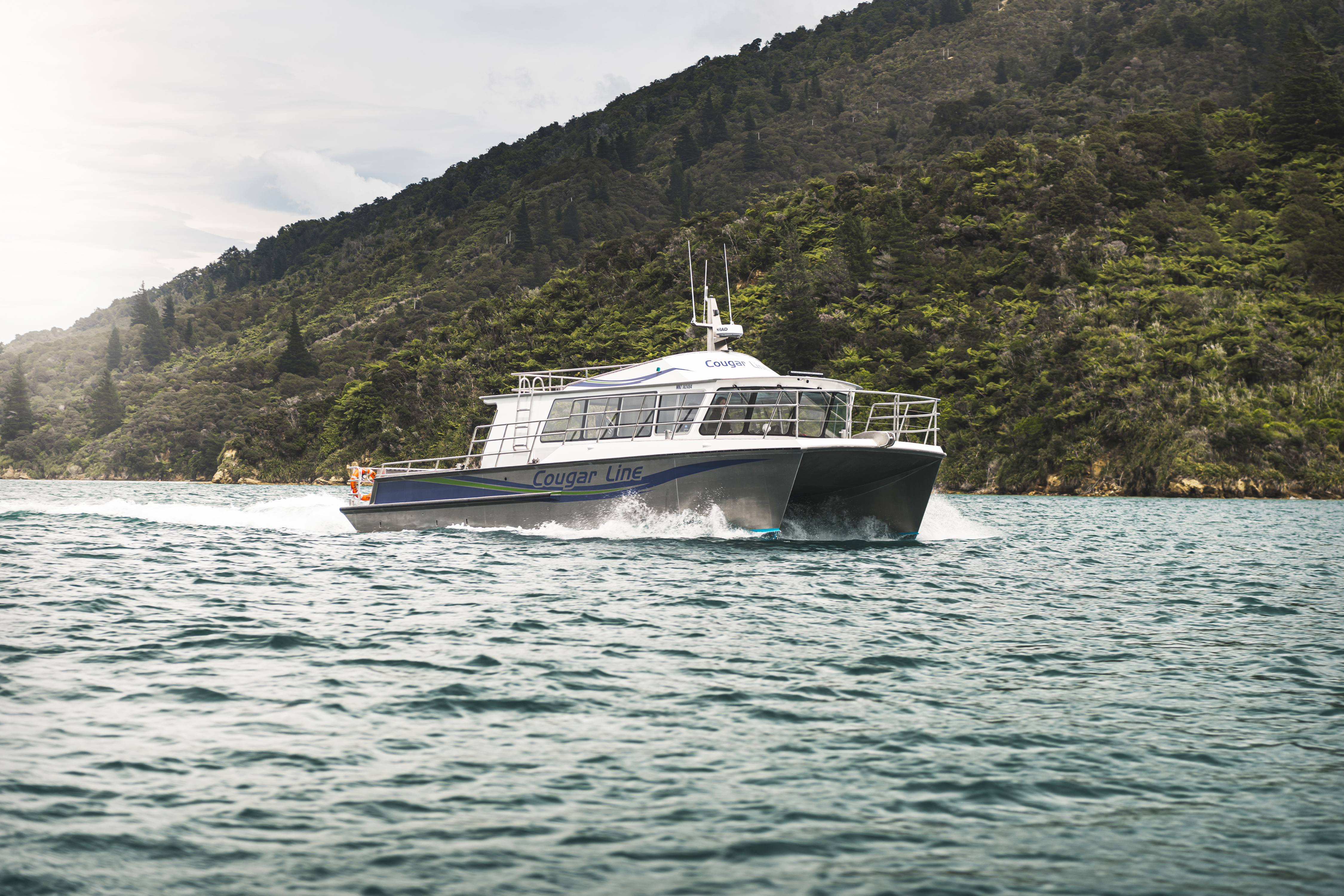 The name on the side of Cougar Line's Sounds Exciting boat sits above the boat's wake, while cruising the Marlborough Sounds, New Zealand