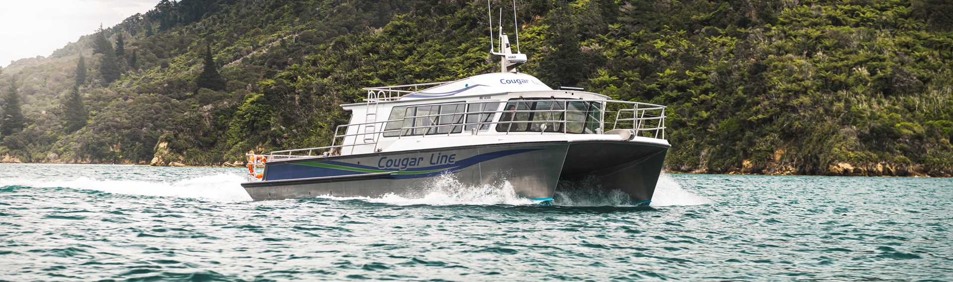 The name on the side of Cougar Line's Sounds Exciting boat sits above the boat's wake, while cruising the Marlborough Sounds, New Zealand