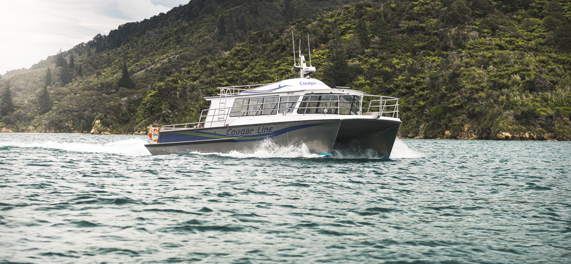 The name on the side of Cougar Line's Sounds Exciting boat sits above the boat's wake, while cruising the Marlborough Sounds, New Zealand