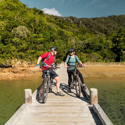 A couple on mountain bikes on the jetty at Ship Cove/Meretoto, Marlborough Sounds, New Zealand.