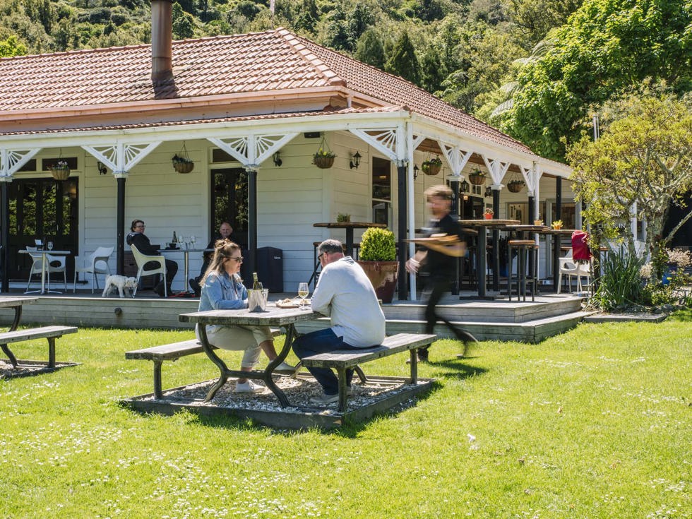 A couple sitting at the lawn picnic table receives food from a waiter in front of the Howden Homestead at the Furneaux Lodge Restaurant in the Marlborough Sounds at the top of New Zealand's South Island 