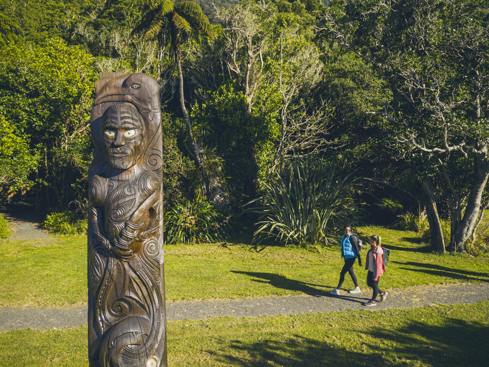 Two people walk at Ship Cove/Meretoto on the northern Queen Charlotte Track in the Marlborough Sounds, New Zealand.