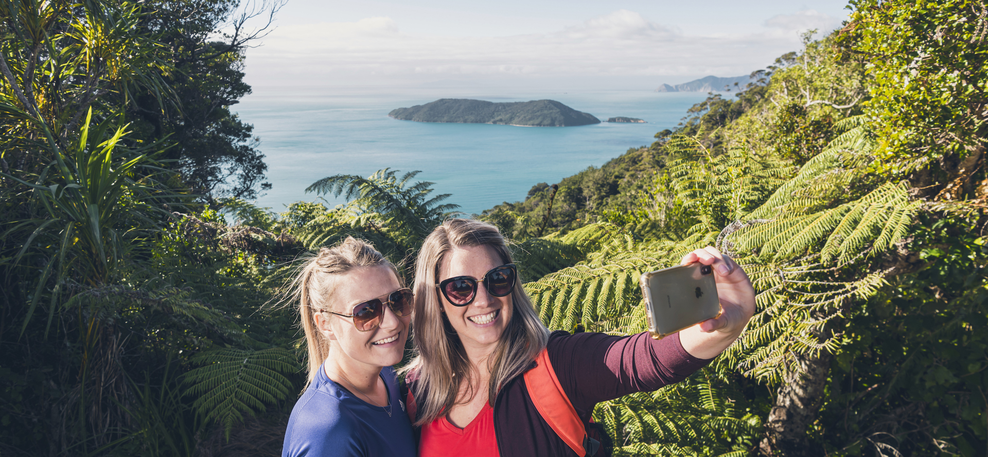 Two women take a selfie at a viewpoint on the northern Queen Charlotte Track in the Marlborough Sounds, New Zealand.