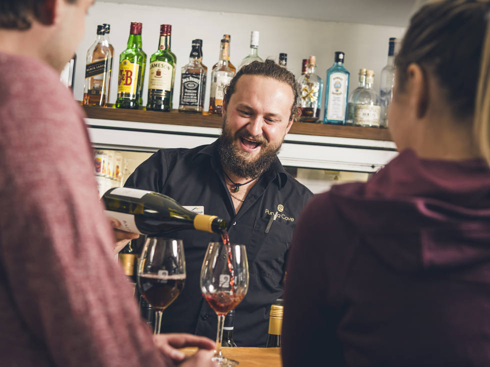 A Punga Cove staff member pours red wine for two people at the Boatshed Café & Bar in the Marlborough Sounds, New Zealand.