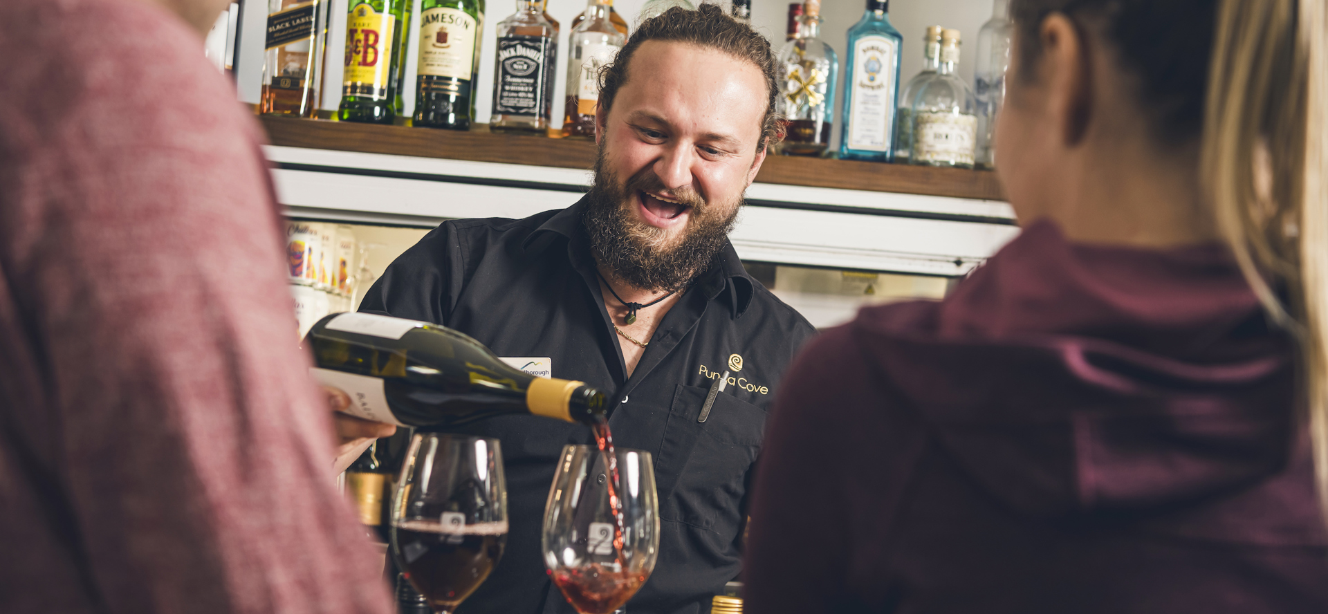 A Punga Cove staff member pours red wine for two people at the Boatshed Café & Bar in the Marlborough Sounds, New Zealand.