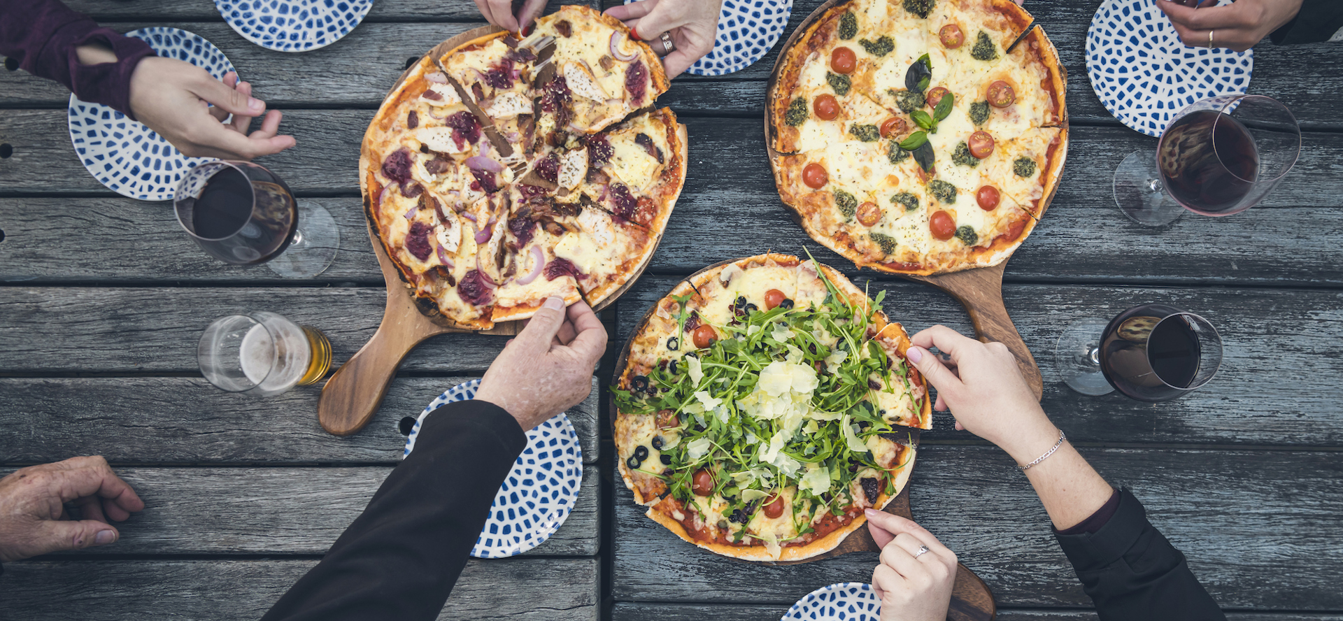 A group of friends share three hot stone baked pizzas and drinks from the Boatshed Cafe and Bar at Punga Cove located in the Marlborough Sounds of New Zealand's South Island