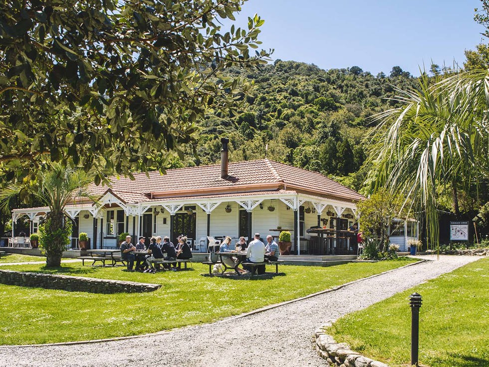 Guests dining outdoors at the lawn picnic tables in front of the Howden Homestead at the Furneaux Lodge Restaurant in the Marlborough Sounds at the top of New Zealand's South Island