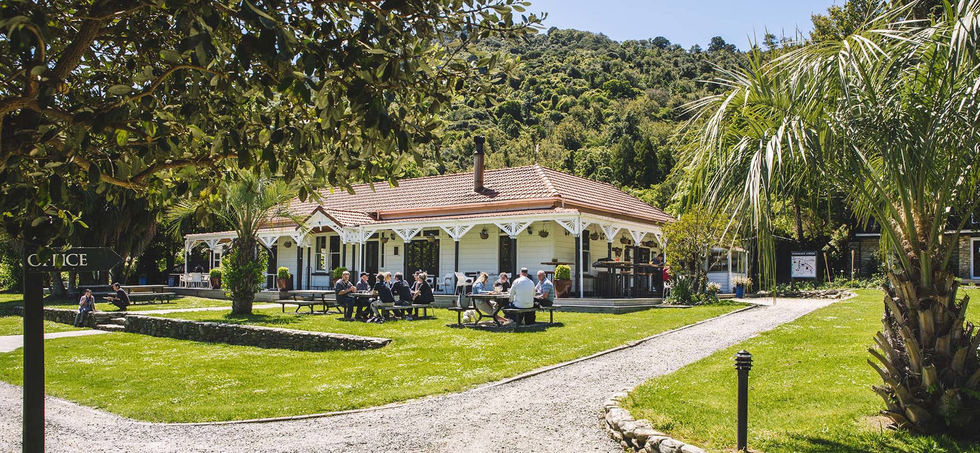 Guests dining outdoors at the lawn picnic tables in front of the Howden Homestead at the Furneaux Lodge Restaurant in the Marlborough Sounds at the top of New Zealand's South Island