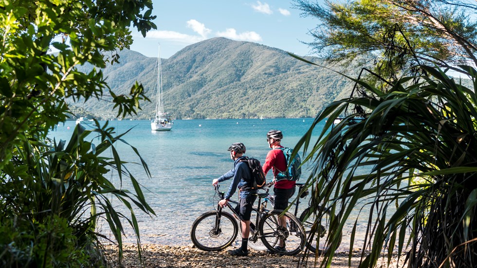 Mountain bikers stop on a beach on the northern Queen Charlotte Track in the Marlborough Sounds, New Zealand.