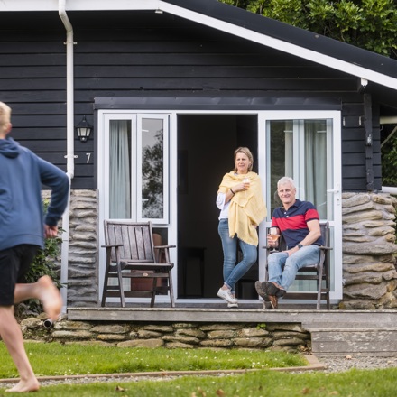 Two children run on the lawn of Furneaux Lodge while their parents watch from a Cook's Cottage with a glass of wine in the Marlborough Sounds, New Zealand.