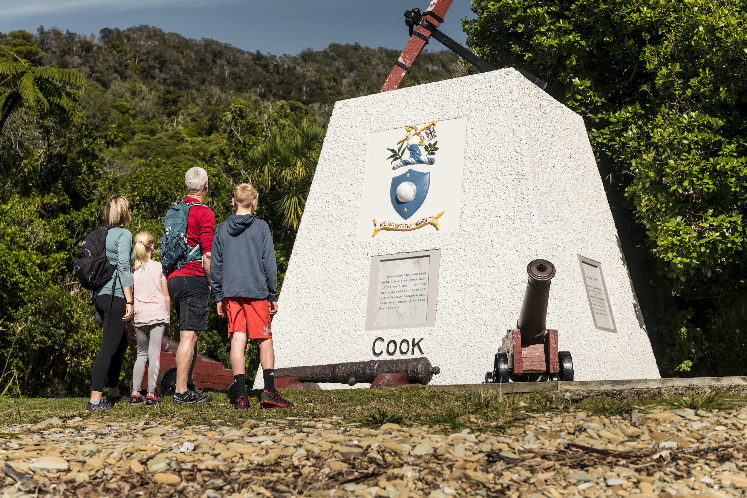 Four people look at the monument to Captain James Cook at Ship Cove/Meretoto in the Marlborough Sounds, New Zealand.