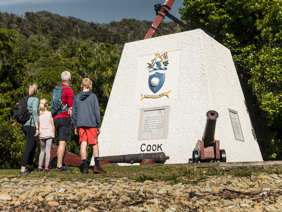 Four people look at the monument to Captain James Cook at Ship Cove/Meretoto in the Marlborough Sounds, New Zealand.