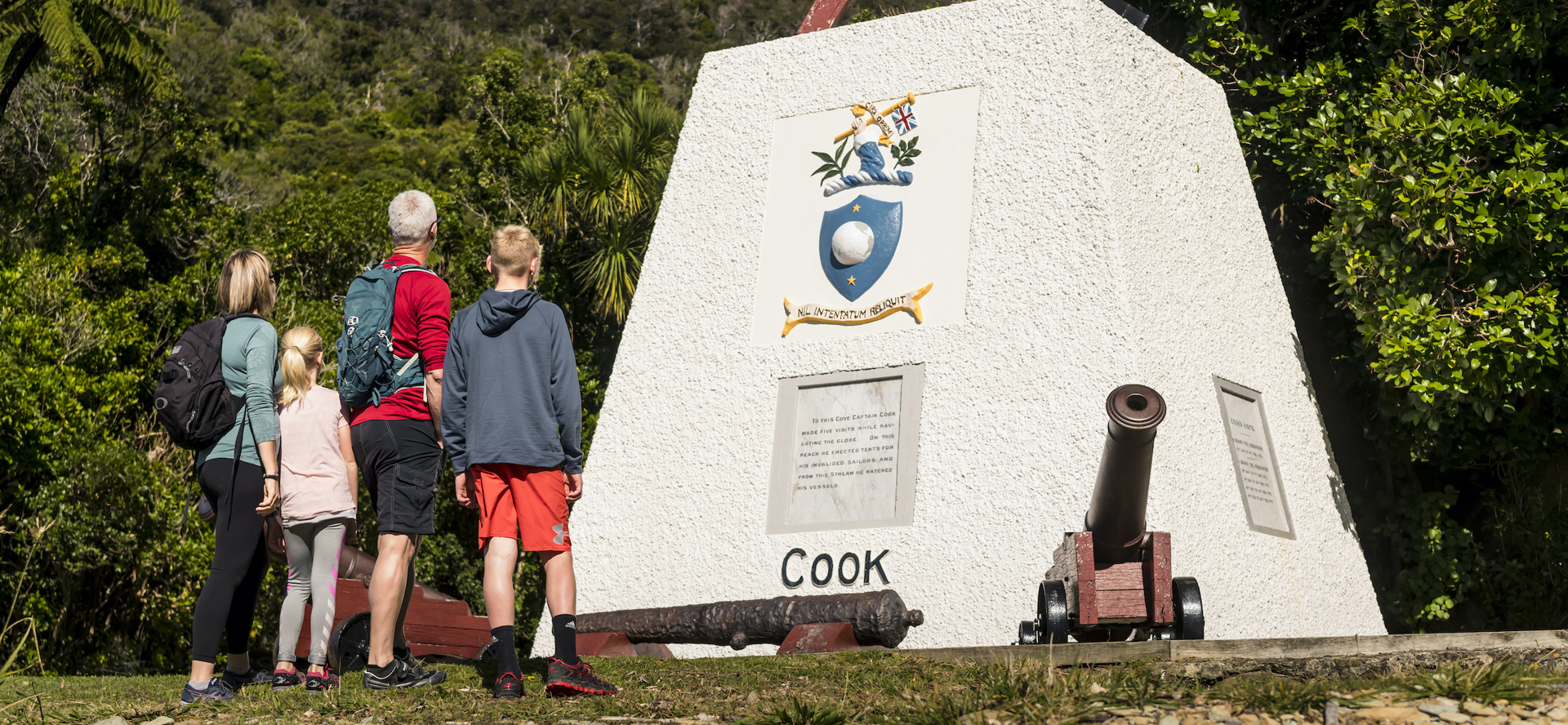 Four people look at the monument to Captain James Cook at Ship Cove/Meretoto in the Marlborough Sounds, New Zealand.