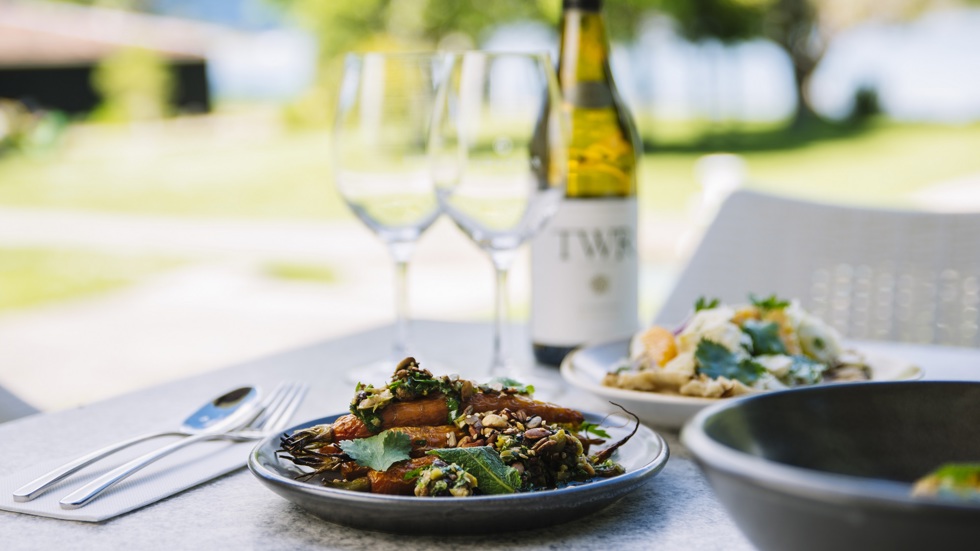 Sharing plates of gourmet vegetables and more served with ocean view and Te Whare Ra wine at Furneaux Lodge in the Marlborough Sounds, New Zealand.