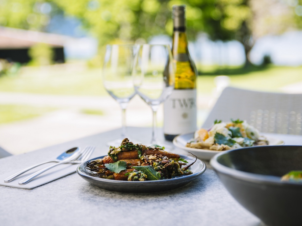 Sharing plates of gourmet vegetables and more served with ocean view and Te Whare Ra wine at Furneaux Lodge in the Marlborough Sounds, New Zealand.