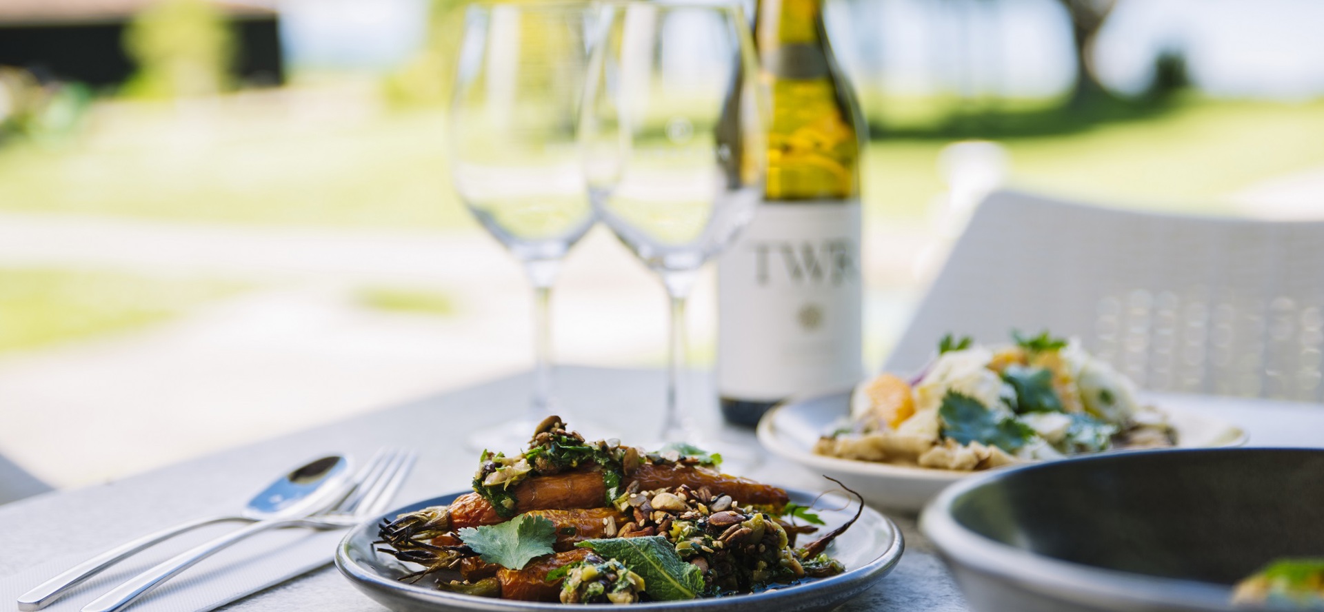 Sharing plates of gourmet vegetables and more served with ocean view and Te Whare Ra wine at Furneaux Lodge in the Marlborough Sounds, New Zealand.