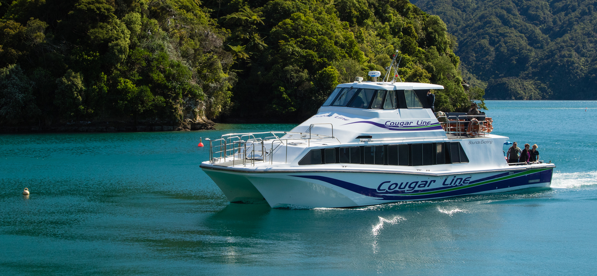 A Cougar Line boat with passengers onboard cruises into a calm bay in the Queen Charlotte Sound/Tōtaranui, Marlborough Sounds, New Zealand.