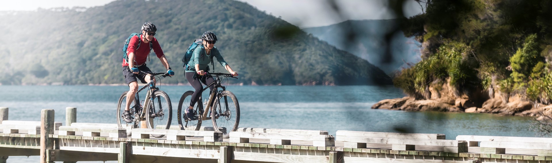 Two mountain bikers on the jetty at Ship Cove/Meretoto, about to start the Queen Charlotte Track in the Marlborough Sounds, New Zealand.