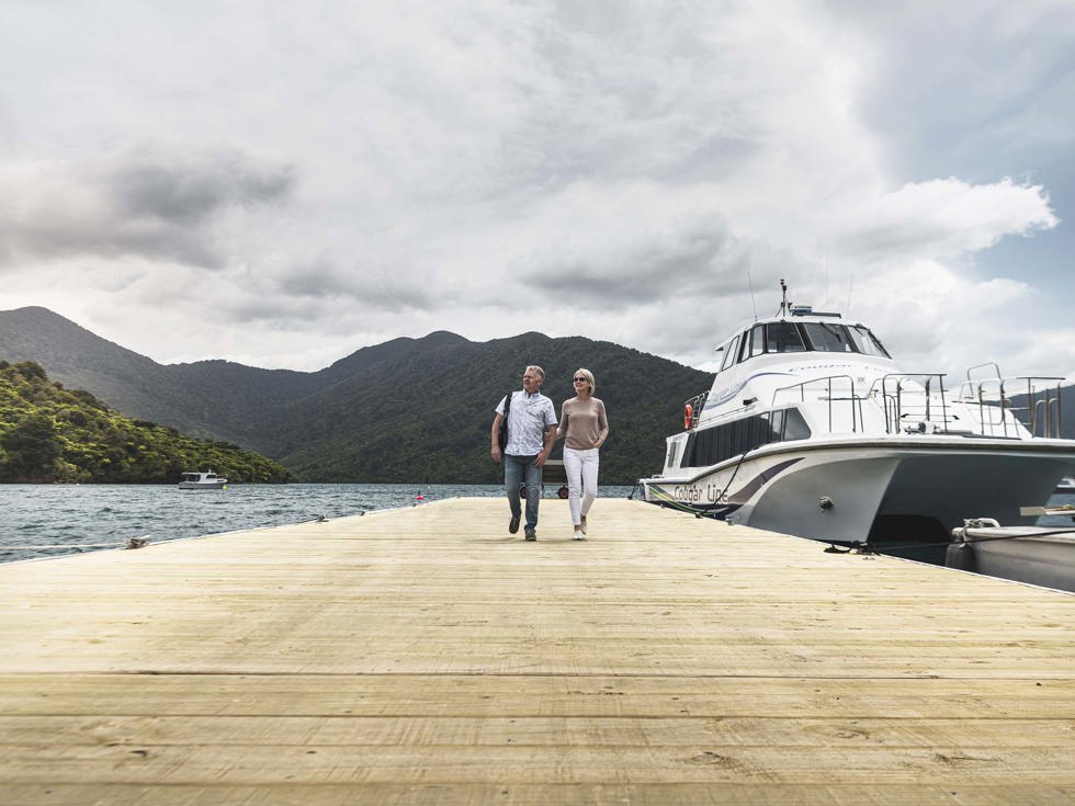 A couple leave Cougar Line vessel from Picton and walk along jetty to Punga Cove in the Marlborough Sounds in New Zealand's top of the South Island