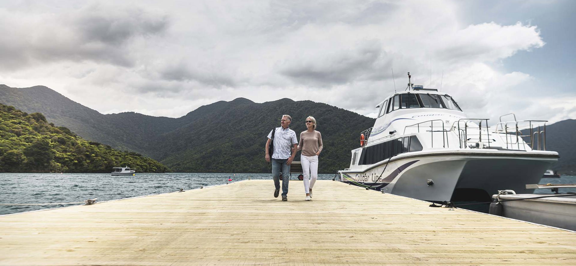 A couple leave Cougar Line vessel from Picton and walk along jetty to Punga Cove in the Marlborough Sounds in New Zealand's top of the South Island