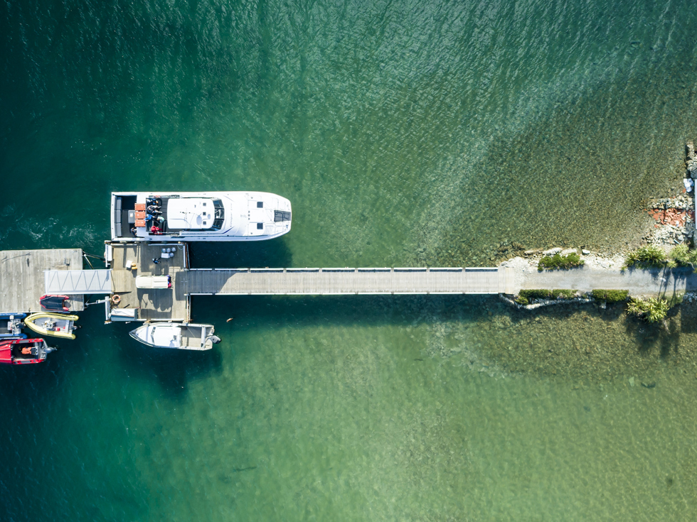 An aerial view of the Furneaux Lodge jetty, boat shed, Cougar Line boat and smaller boats in the Marlborough Sounds, New Zealand.