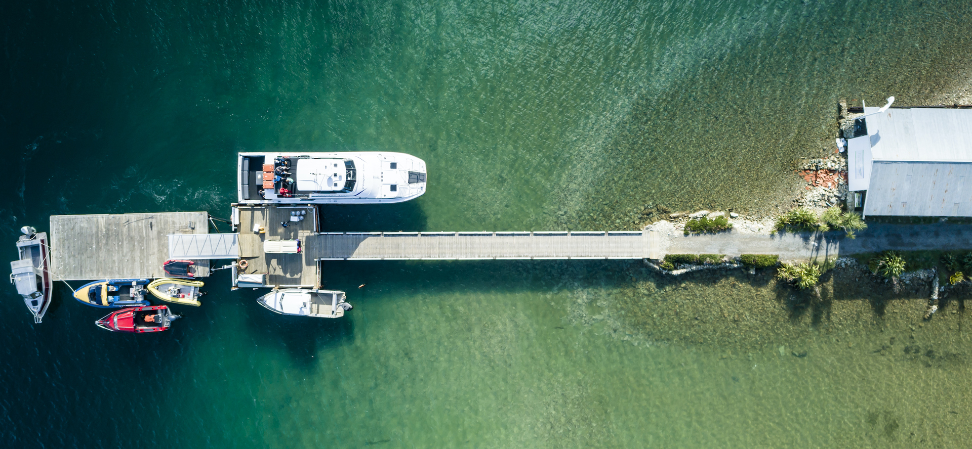 An aerial view of the Furneaux Lodge jetty, boat shed, Cougar Line boat and smaller boats in the Marlborough Sounds, New Zealand.