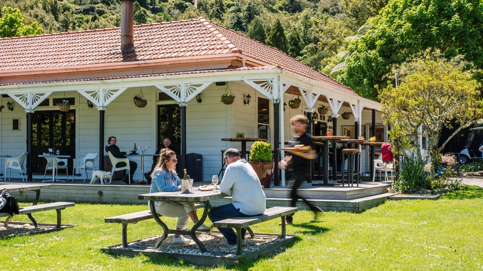 Two people are served by a waiter on the lawn while dining at Furneaux Lodge in the Marlborough Sounds, New Zealand.