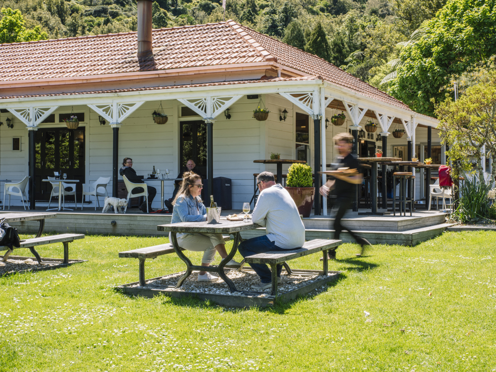 Two people are served by a waiter on the lawn while dining at Furneaux Lodge in the Marlborough Sounds, New Zealand.