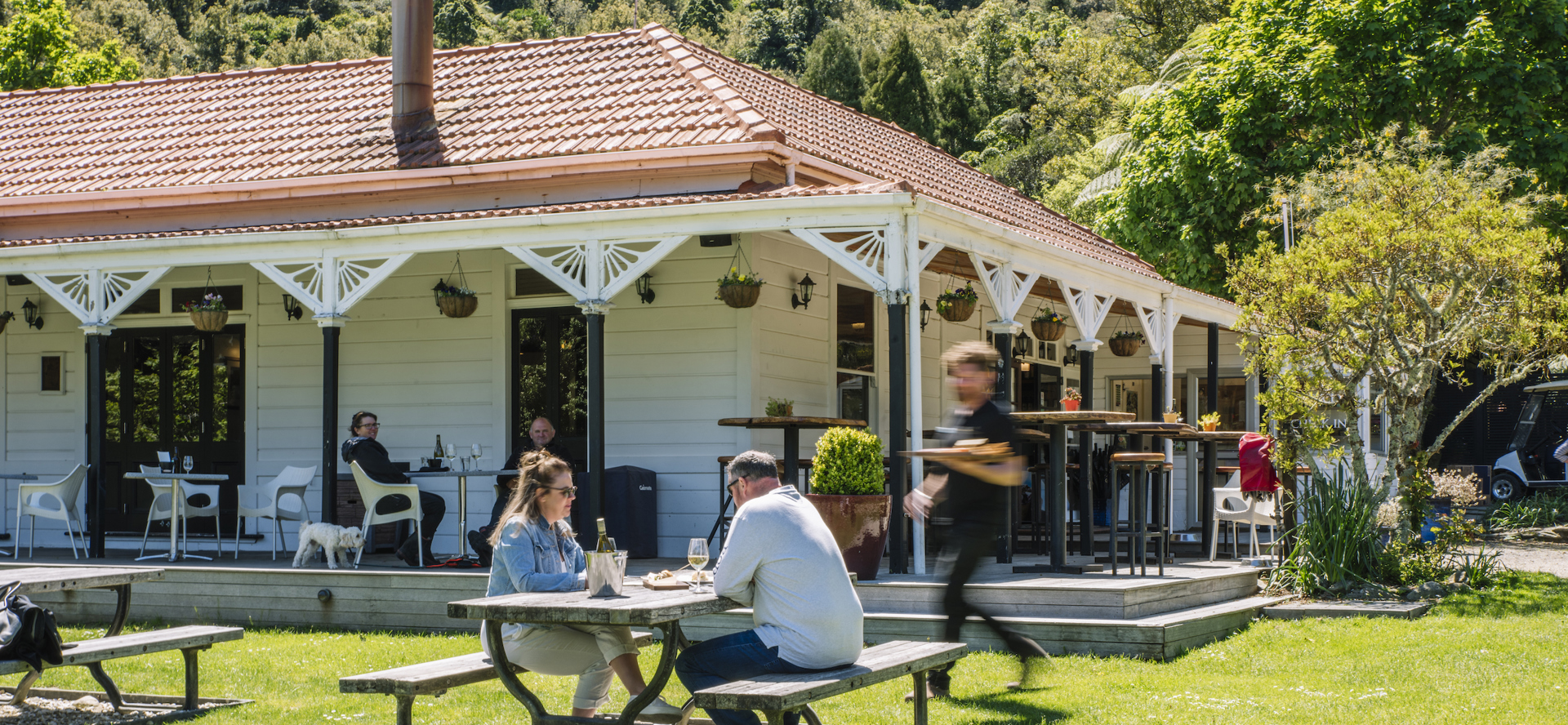 Two people are served by a waiter on the lawn while dining at Furneaux Lodge in the Marlborough Sounds, New Zealand.